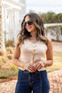 Woman wearing a beige top with gold buttons and blue jeans outdoors.