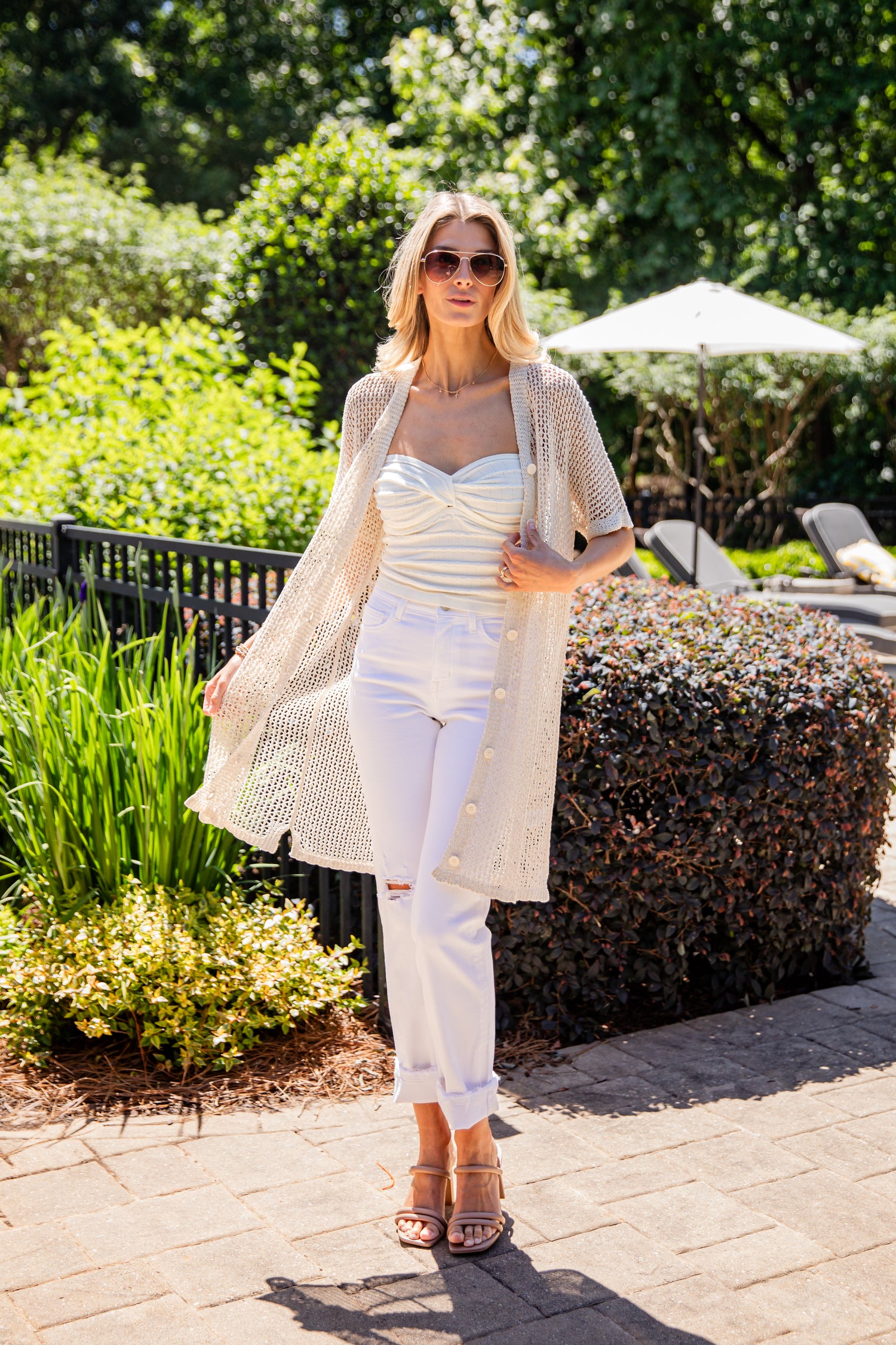 Woman in a white outfit standing outdoors with greenery in the background