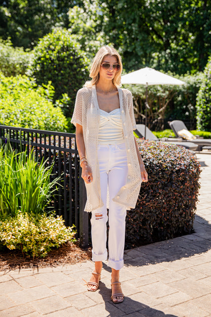 Woman in a white outfit standing outdoors with greenery and a pool area in the background