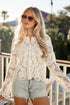 Woman wearing a lace top and denim shorts on a balcony with palm trees in the background