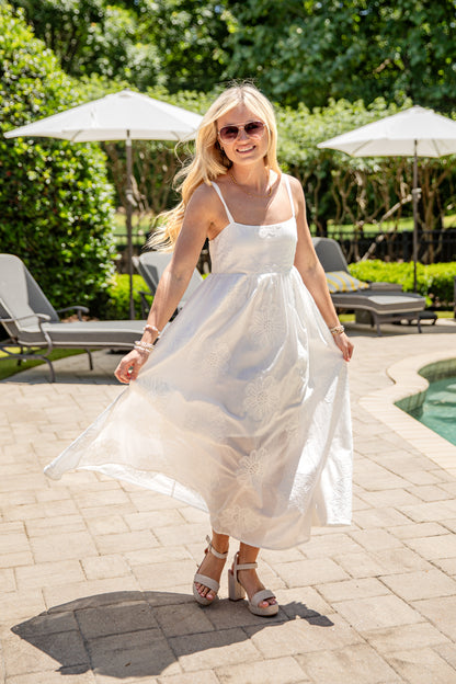 Woman in a white dress standing by a pool with greenery in the background