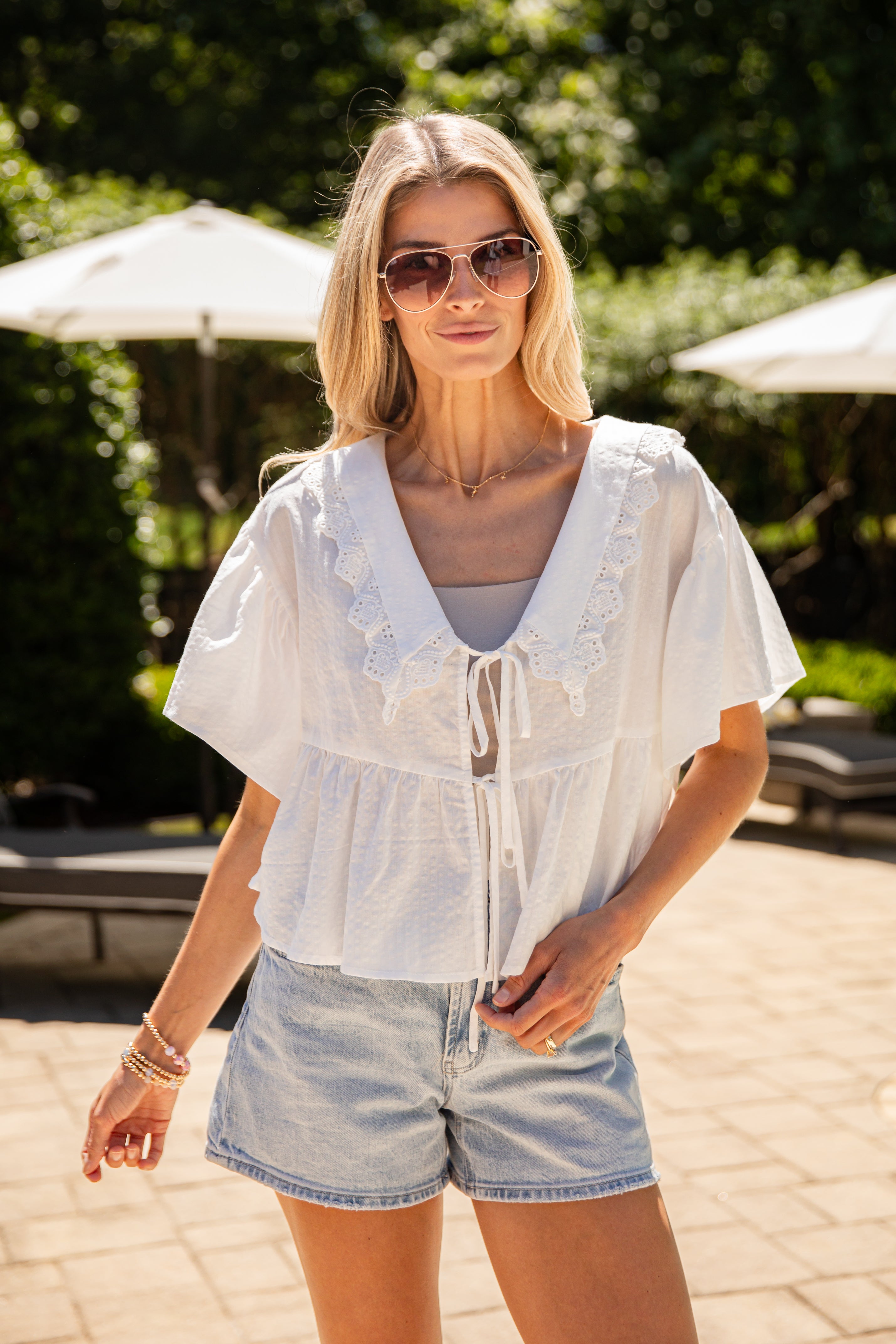 Woman wearing a light blue blouse and denim shorts outdoors with greenery in the background