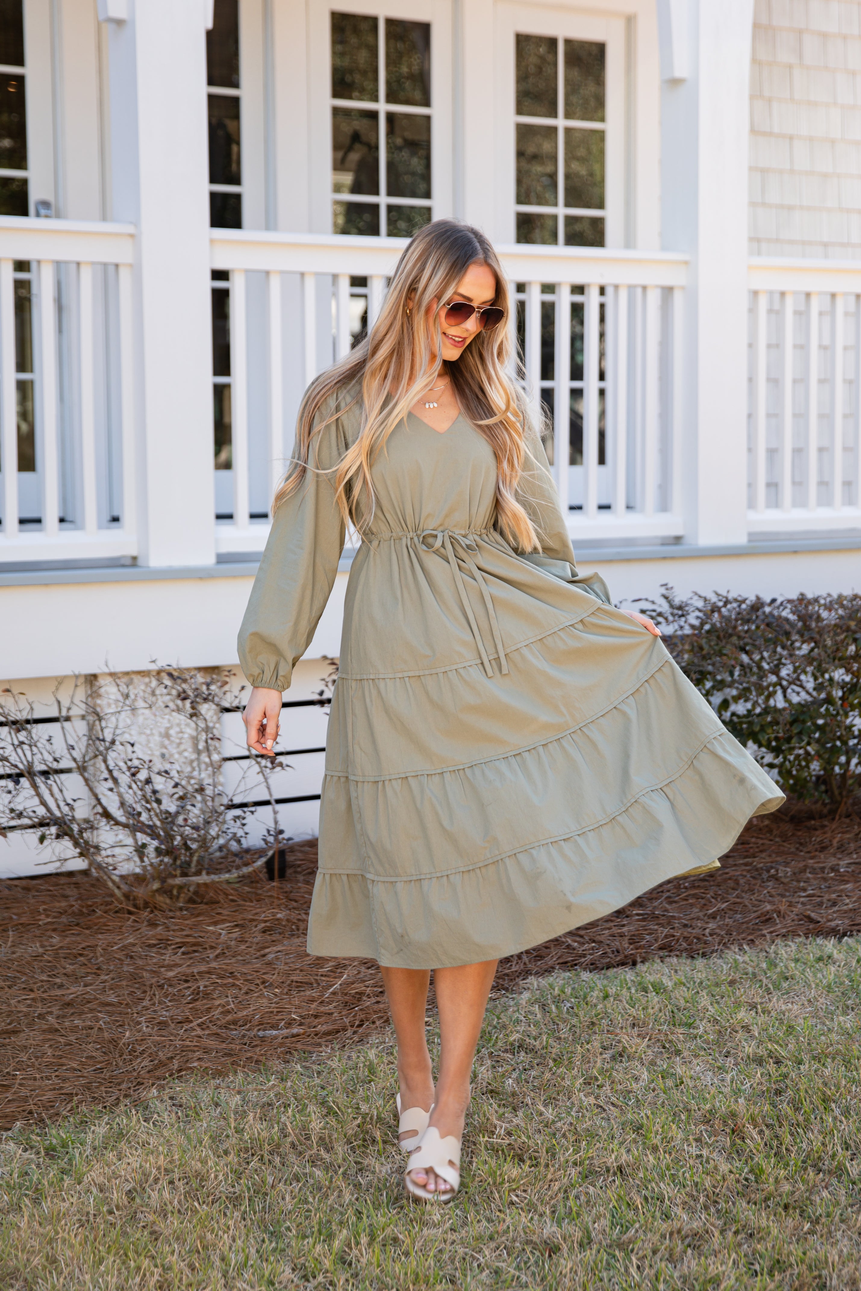 Woman in a long, light green dress standing outdoors with a house in the background