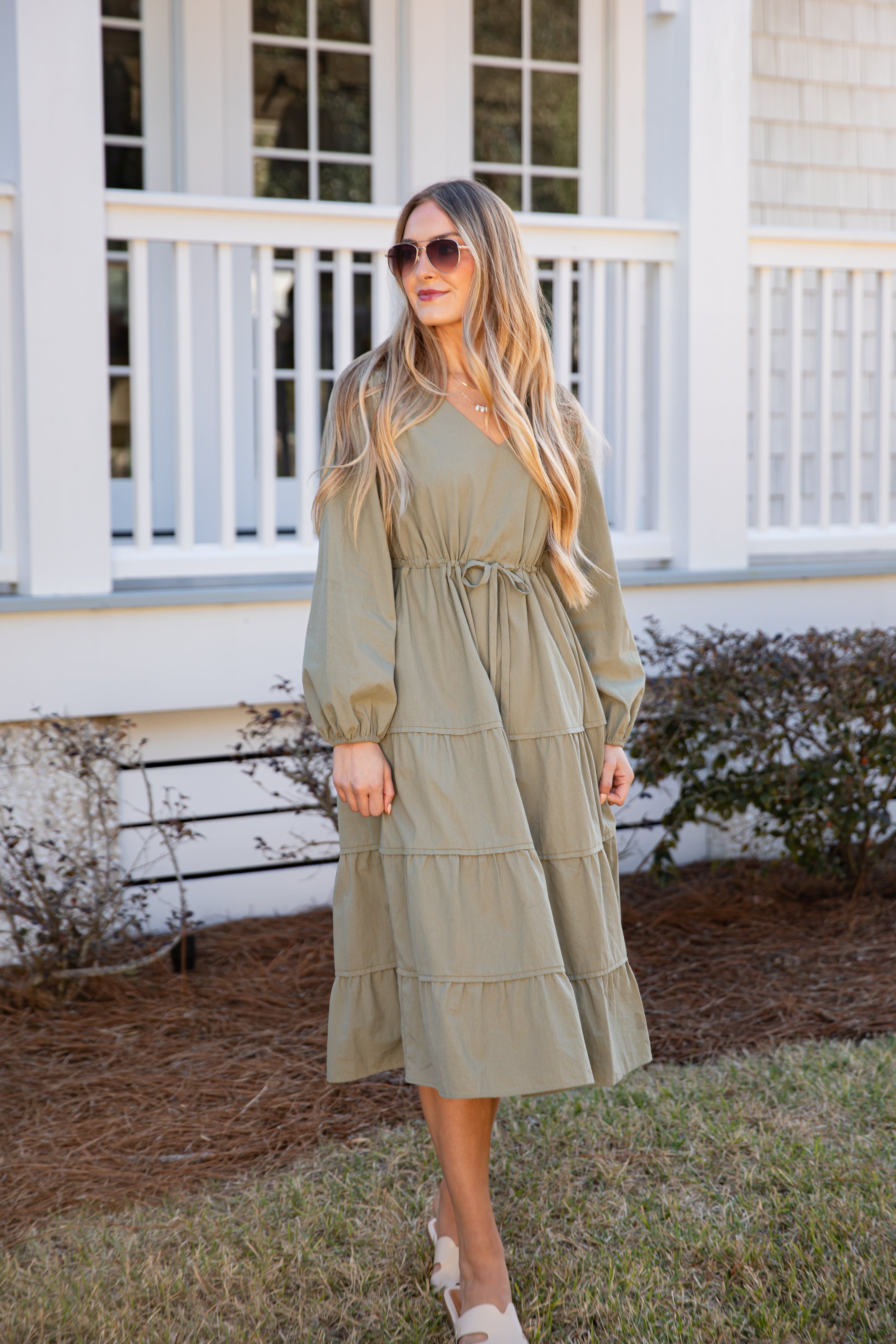 Woman wearing a green dress standing in front of a house.