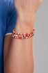 Close-up of a wrist wearing a red, white, and gold beaded bracelet on a gray background.