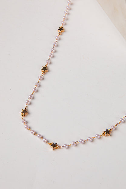 A delicate necklace featuring small light pink pearls and gold star-shaped charms, displayed on a clean off-white surface.