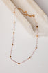 A delicate necklace with small pale pink beads and gold star-shaped accents, draped over a cream-colored fabric prop on a light background.