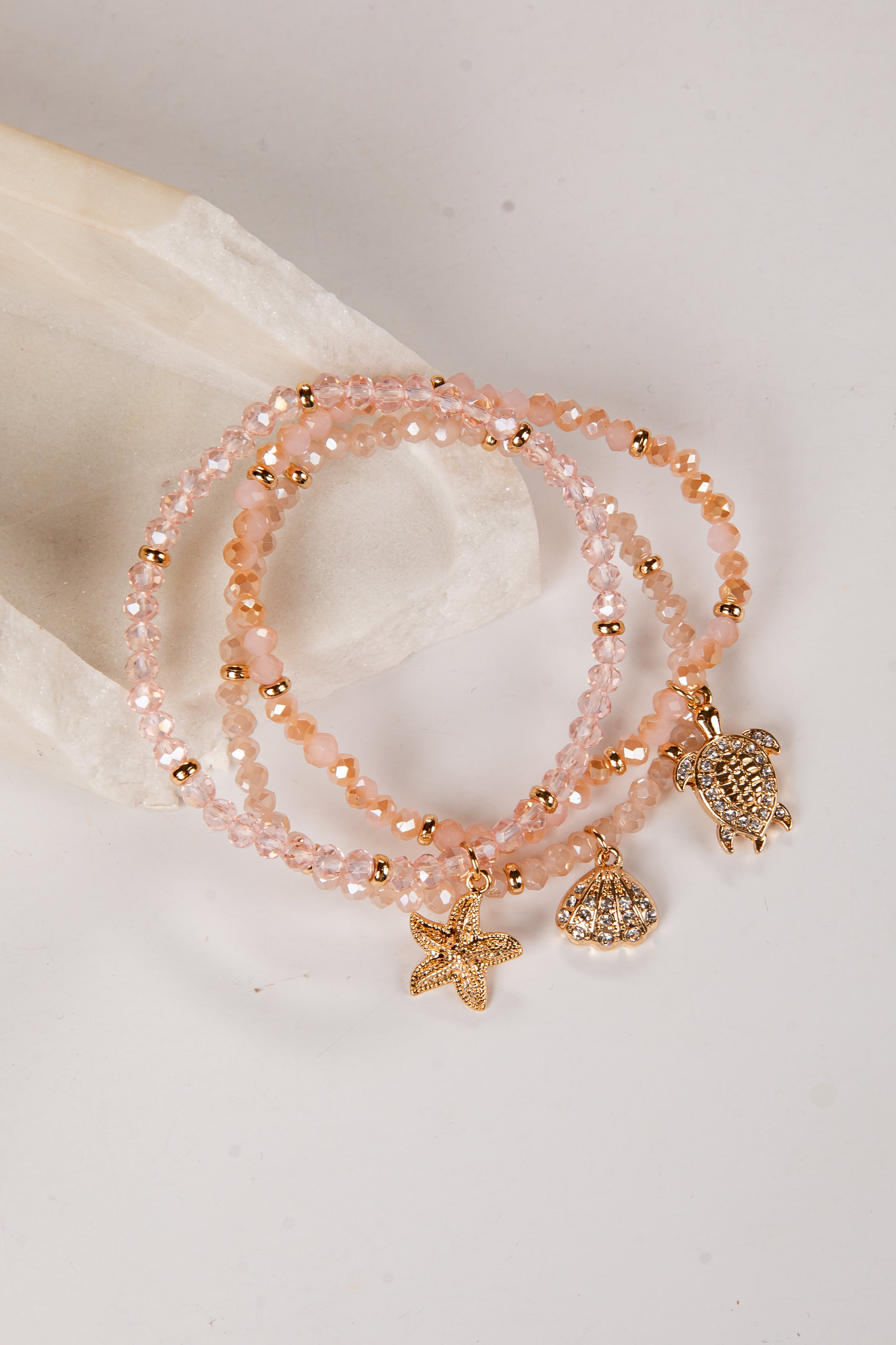 Set of pink beaded bracelets with charms on a white surface