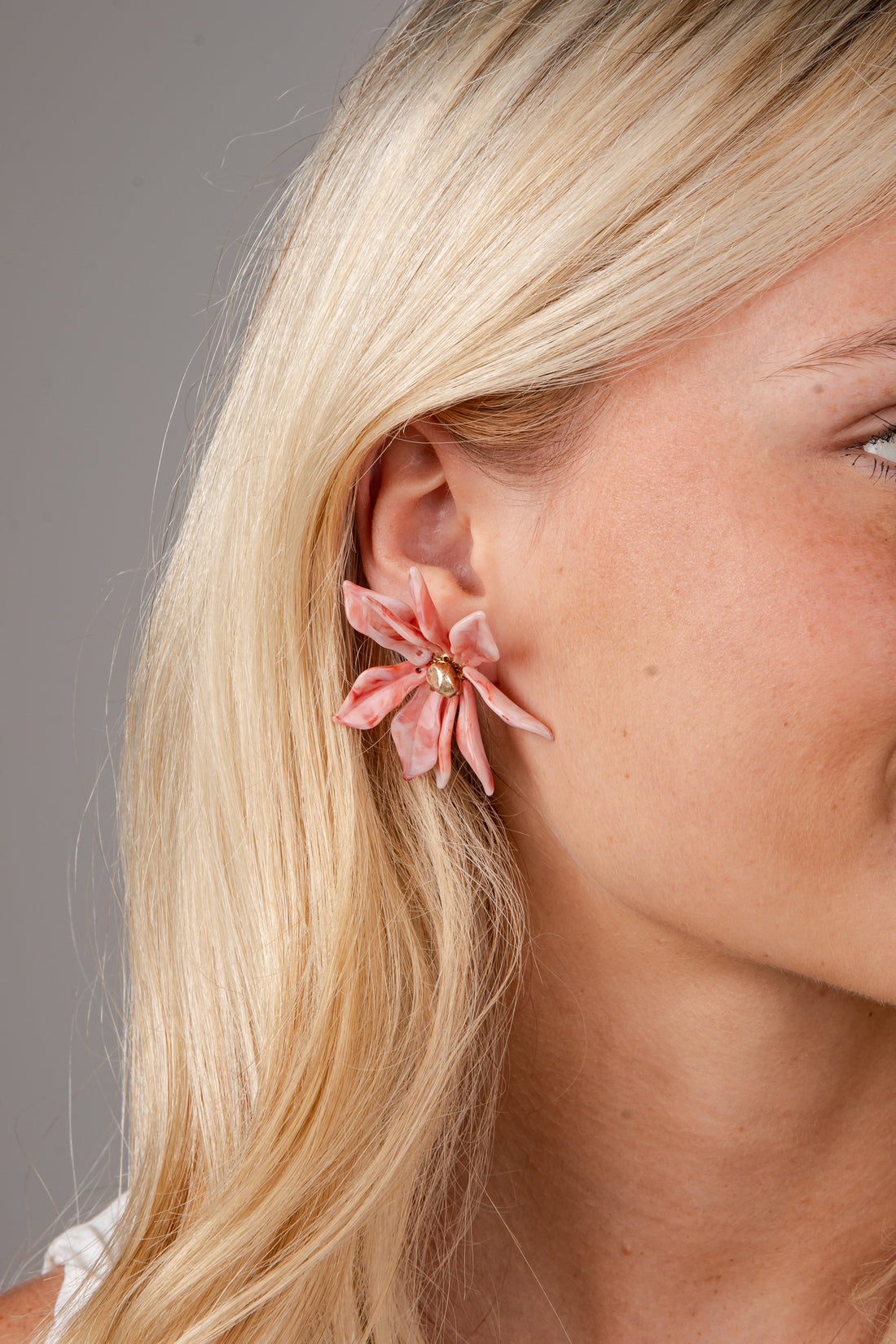 Close-up of a woman wearing a pink floral earring against a neutral background
