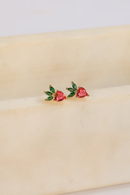 Heart-shaped earrings with green and red stones on a beige surface