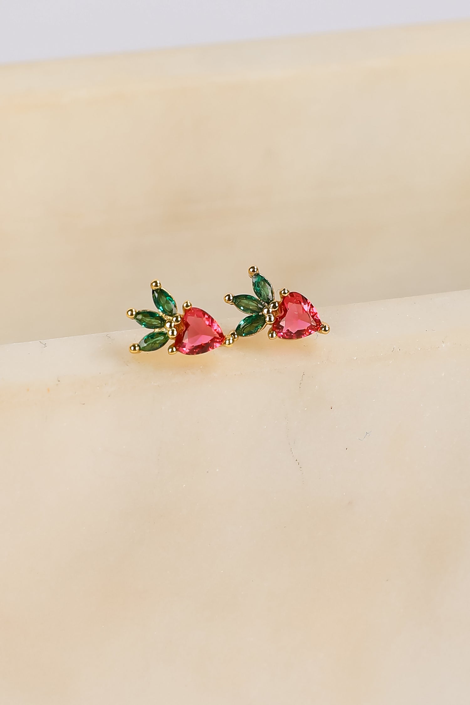 Pair of earrings with heart-shaped gemstones on a beige surface