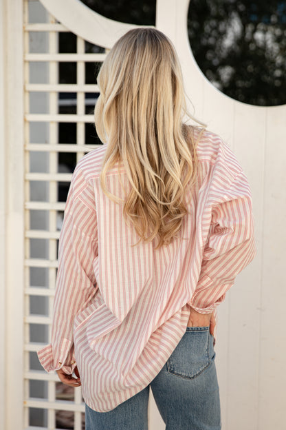 Person wearing a pink and white striped shirt and blue jeans standing in front of a white lattice door.