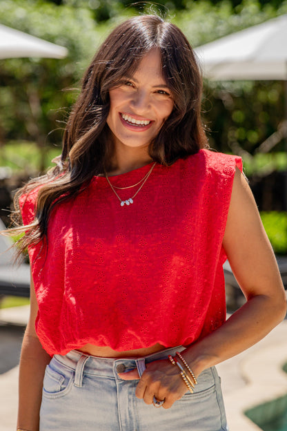 Woman wearing a red top and light blue jeans standing by a pool with greenery in the background