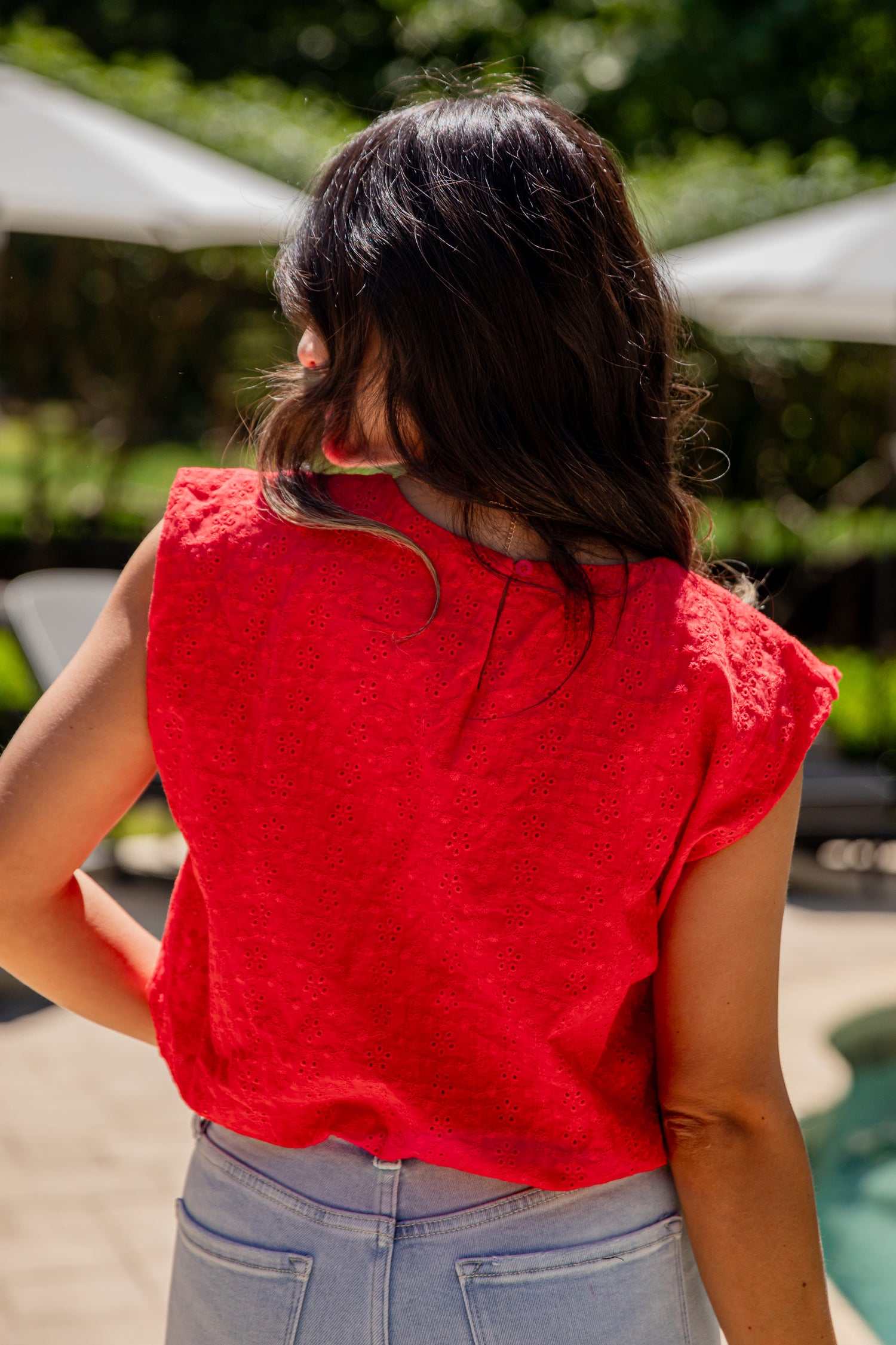 Person wearing a red sleeveless top and blue jeans standing outdoors with blurred background