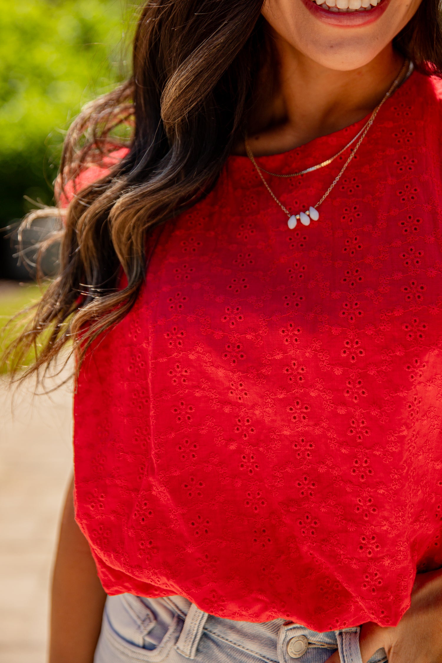 Woman wearing a red perforated top with a blurred outdoor background