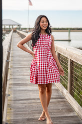 Woman in a red and white checkered dress standing on a wooden dock by a body of water.