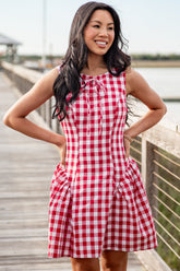 Woman wearing a red and white checkered dress standing on a wooden dock by a body of water.