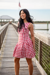 Woman in a red and white checkered dress standing on a wooden pier.