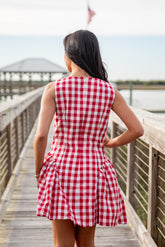 Woman in a red and white checkered dress standing on a wooden boardwalk by a waterfront.