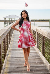 Woman in a red and white checkered dress standing on a wooden dock by a body of water.