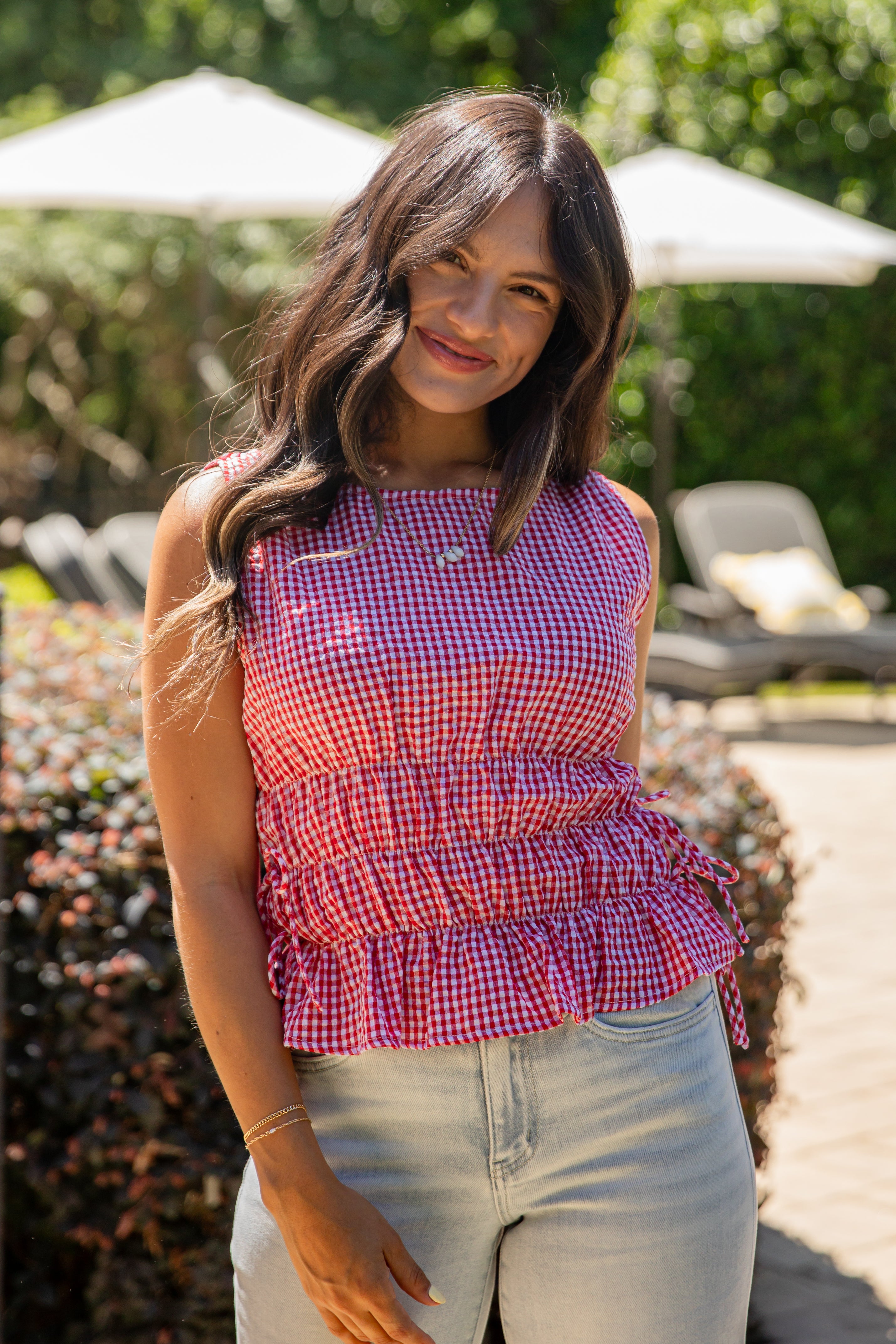 Woman wearing a red and white checkered top and light blue jeans standing outdoors.