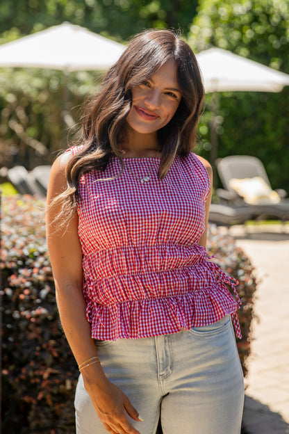 Woman wearing a red and white checkered top and light blue jeans standing outdoors.