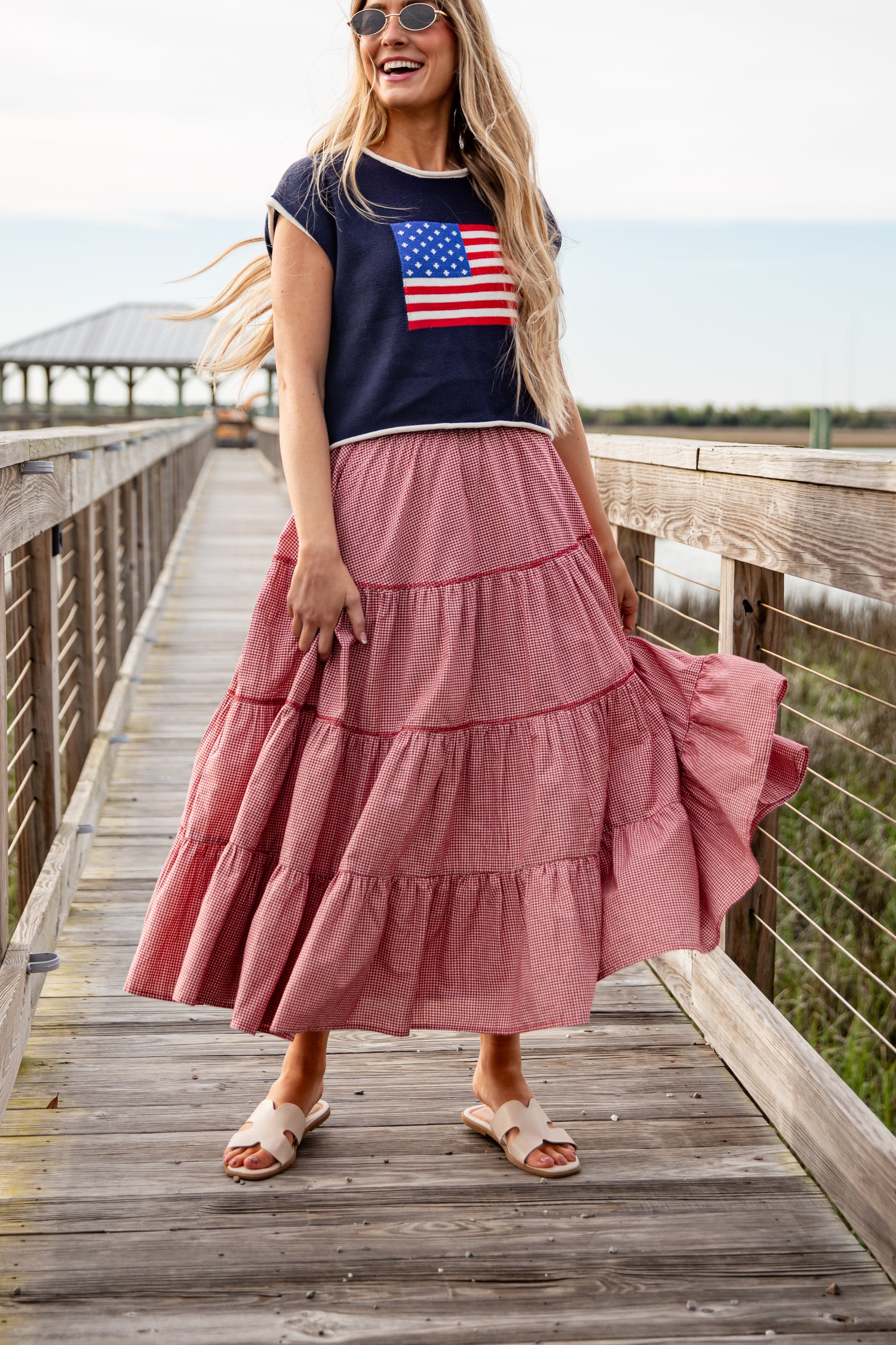 Woman wearing a navy t-shirt with an American flag design and a pink tiered skirt on a wooden boardwalk.