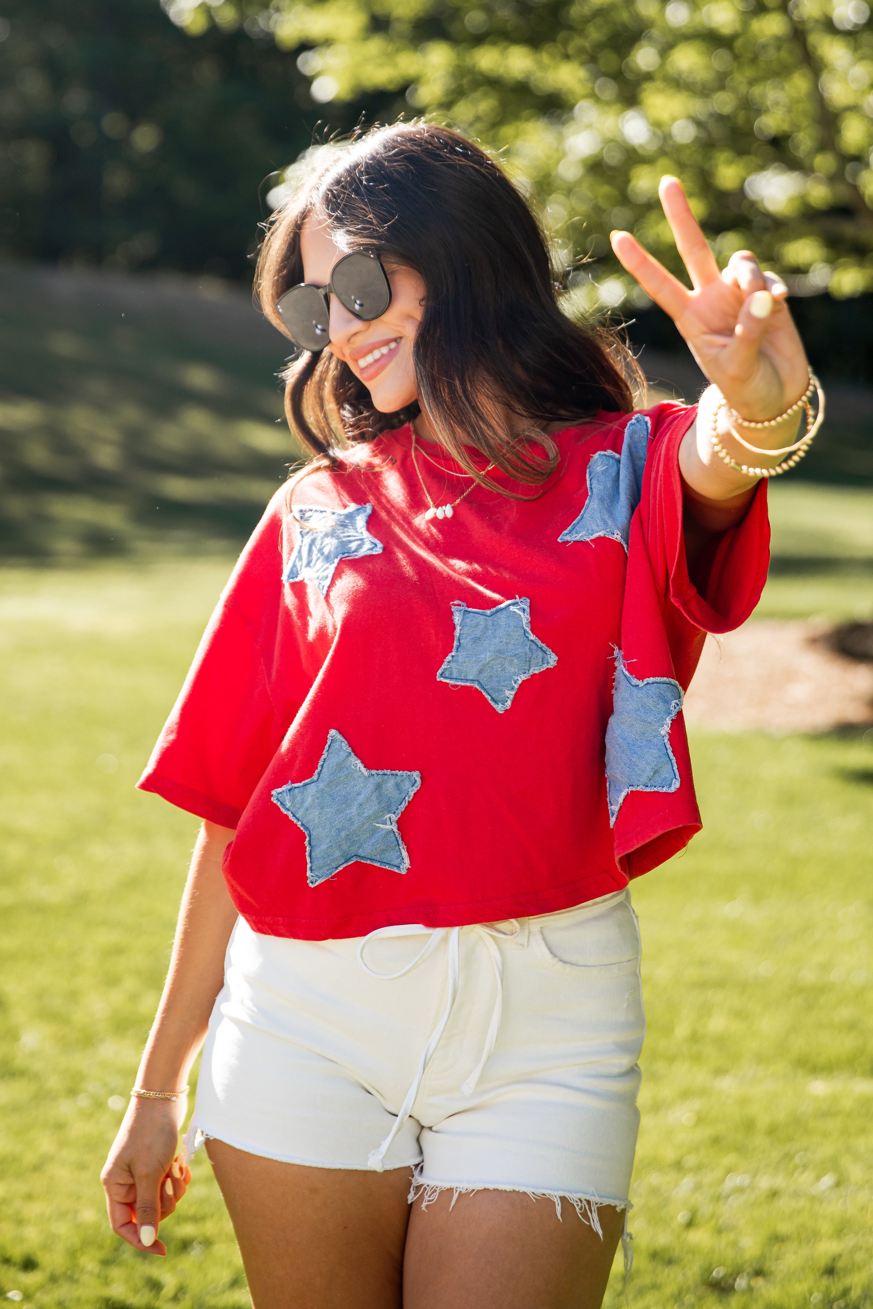 Woman wearing a red shirt with blue star patterns and white shorts, standing outdoors.