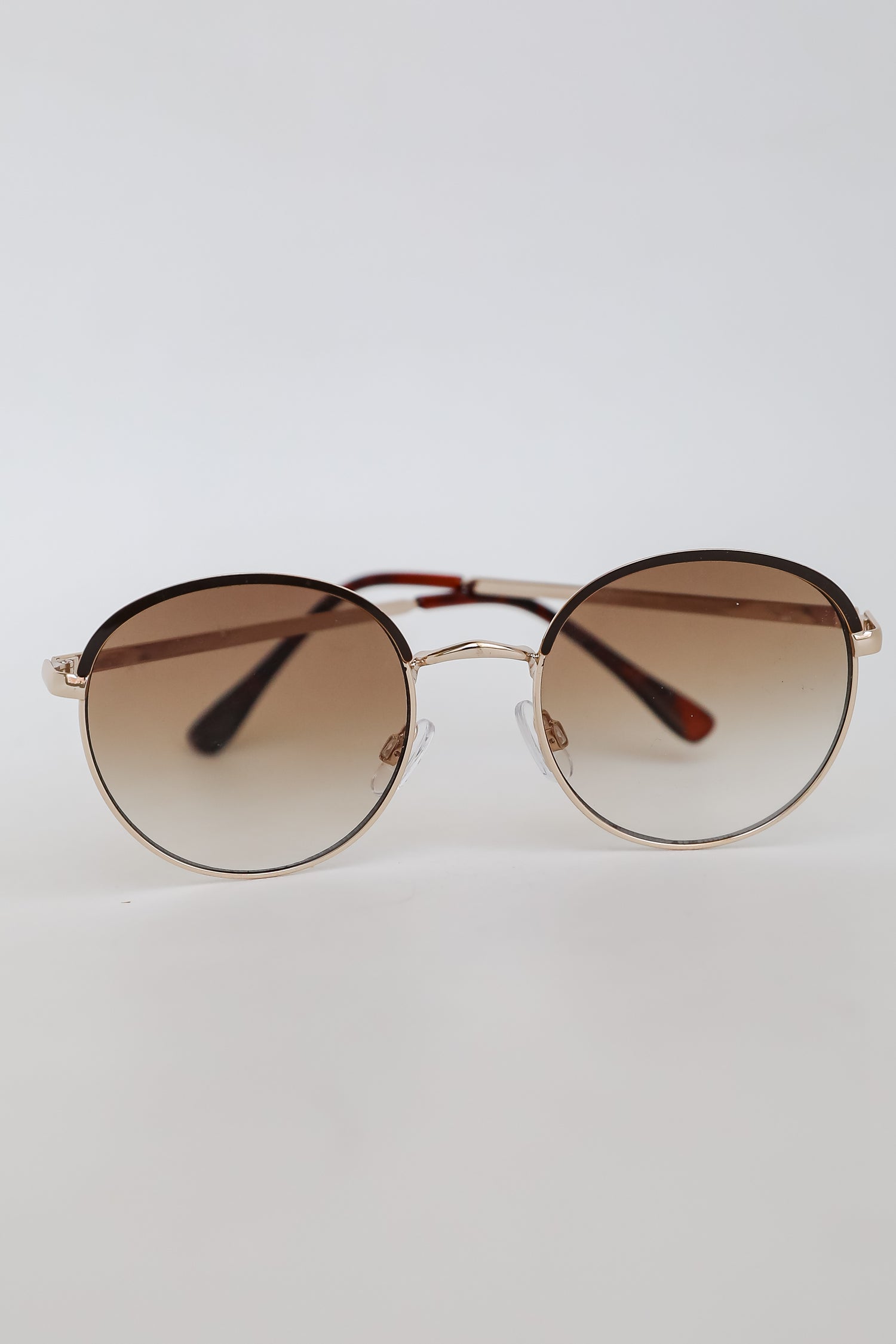 Round sunglasses with gold frame and brown gradient lenses on a light gray background