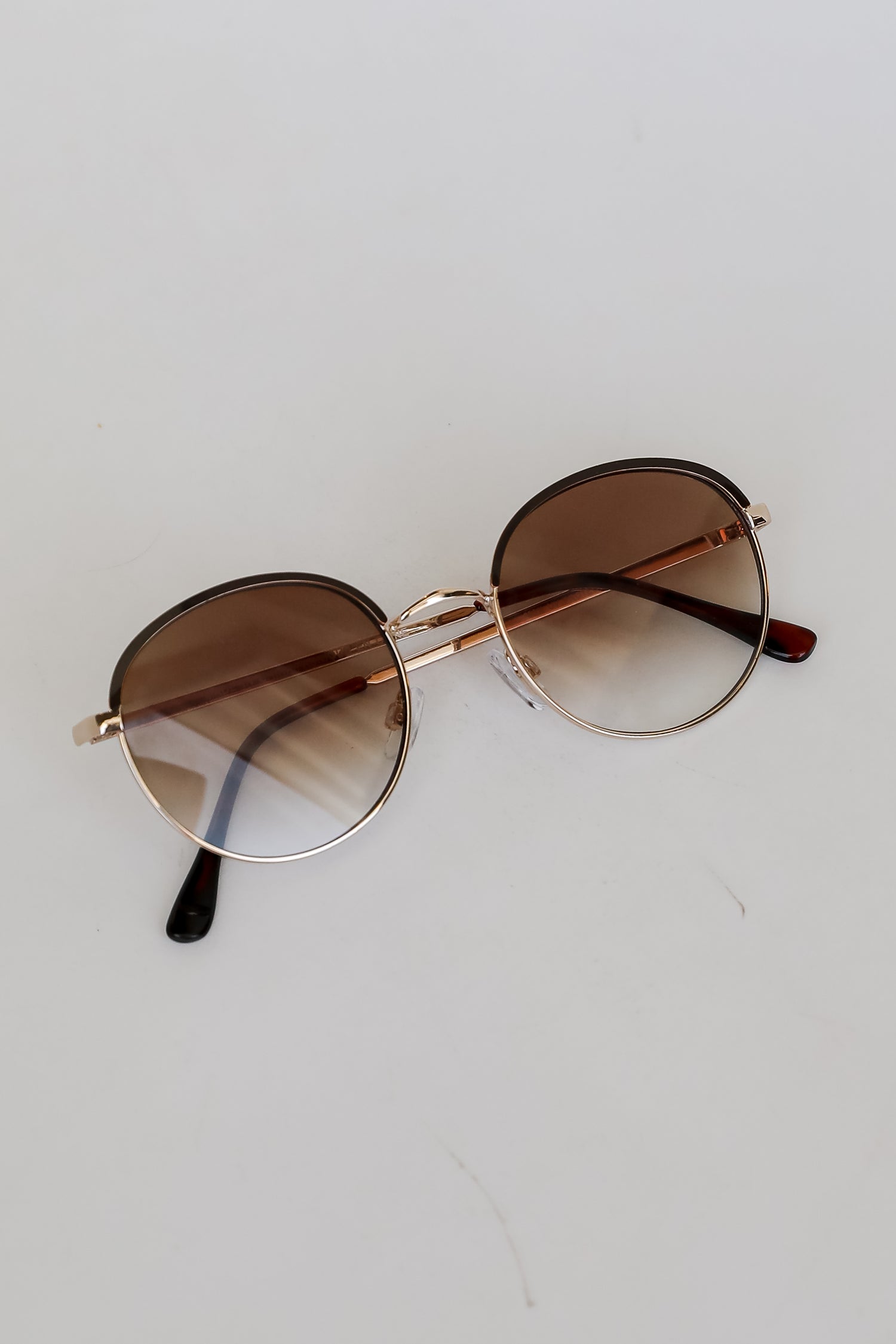 Round sunglasses with gold frame and brown lenses on a white background