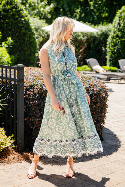Woman in a floral dress standing outdoors with greenery and a pool area in the background