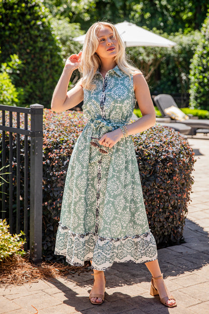 Woman in a floral dress standing outdoors with greenery and a pool area in the background