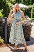 Woman in a floral dress standing outdoors with greenery and a pool area in the background