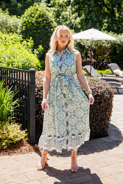 Woman in a floral dress standing outdoors with greenery and a pool area in the background