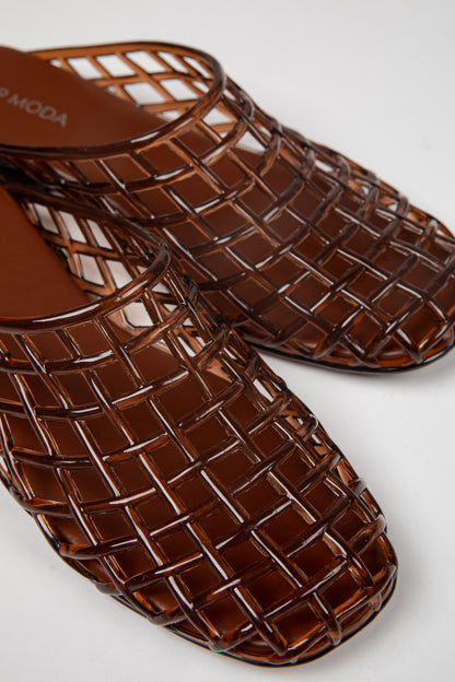 A pair of glossy brown woven mesh mule sandals with a square toe, shown on a clean white background. The brand name &