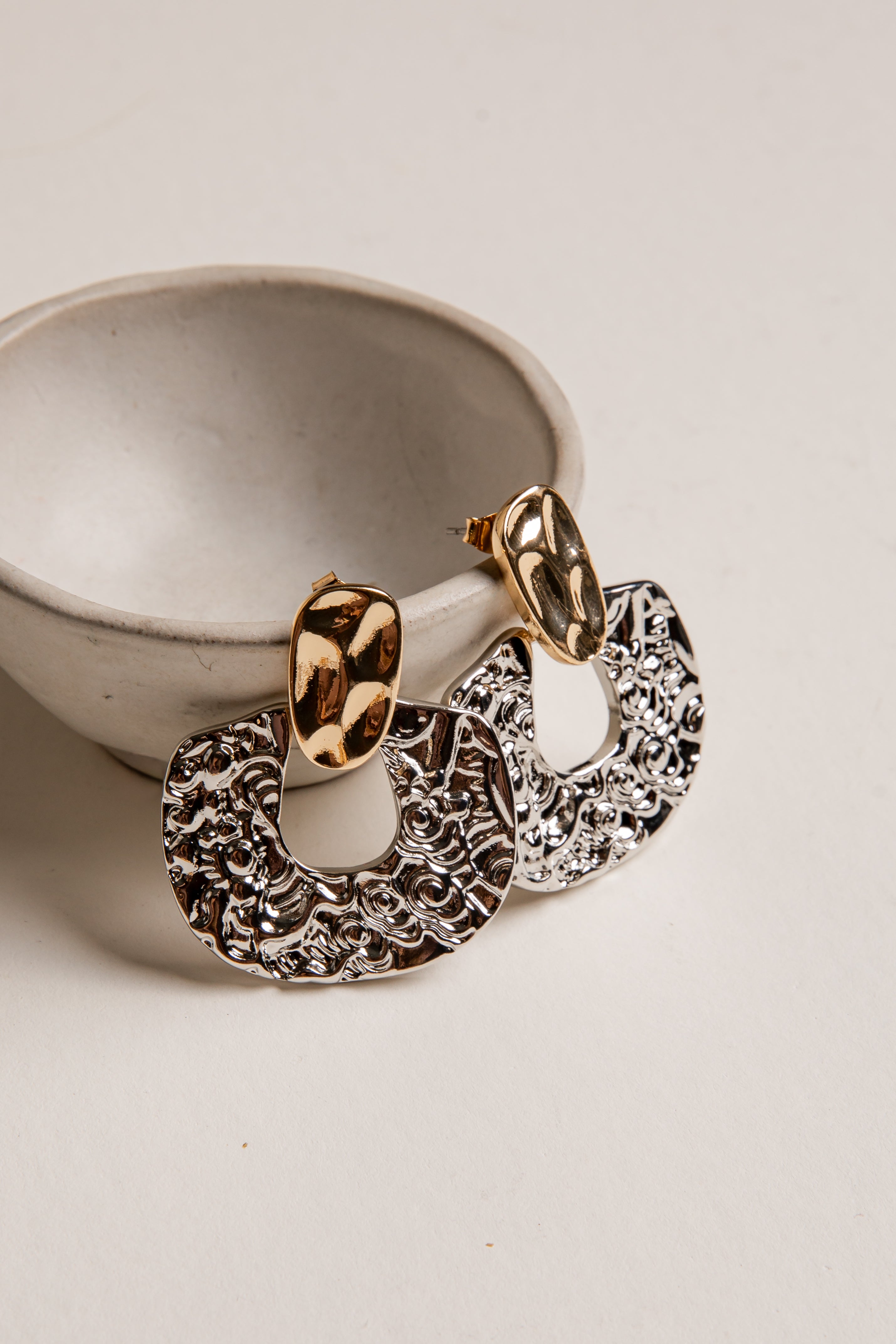 Gold and silver hoop earrings on a white surface with a neutral background