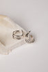 A pair of silver-toned multi-band hoop earrings resting on a textured beige stone slab against a clean white background.