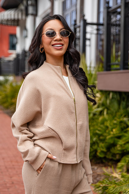 Woman wearing a beige outfit with sunglasses in an outdoor setting