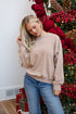 Woman in beige sweater and blue jeans standing in front of a decorated Christmas tree.