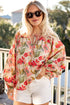Woman wearing a floral blouse and white shorts on a balcony with greenery in the background