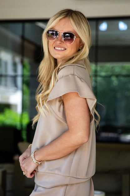 Woman wearing sunglasses and a beige outfit in an outdoor setting