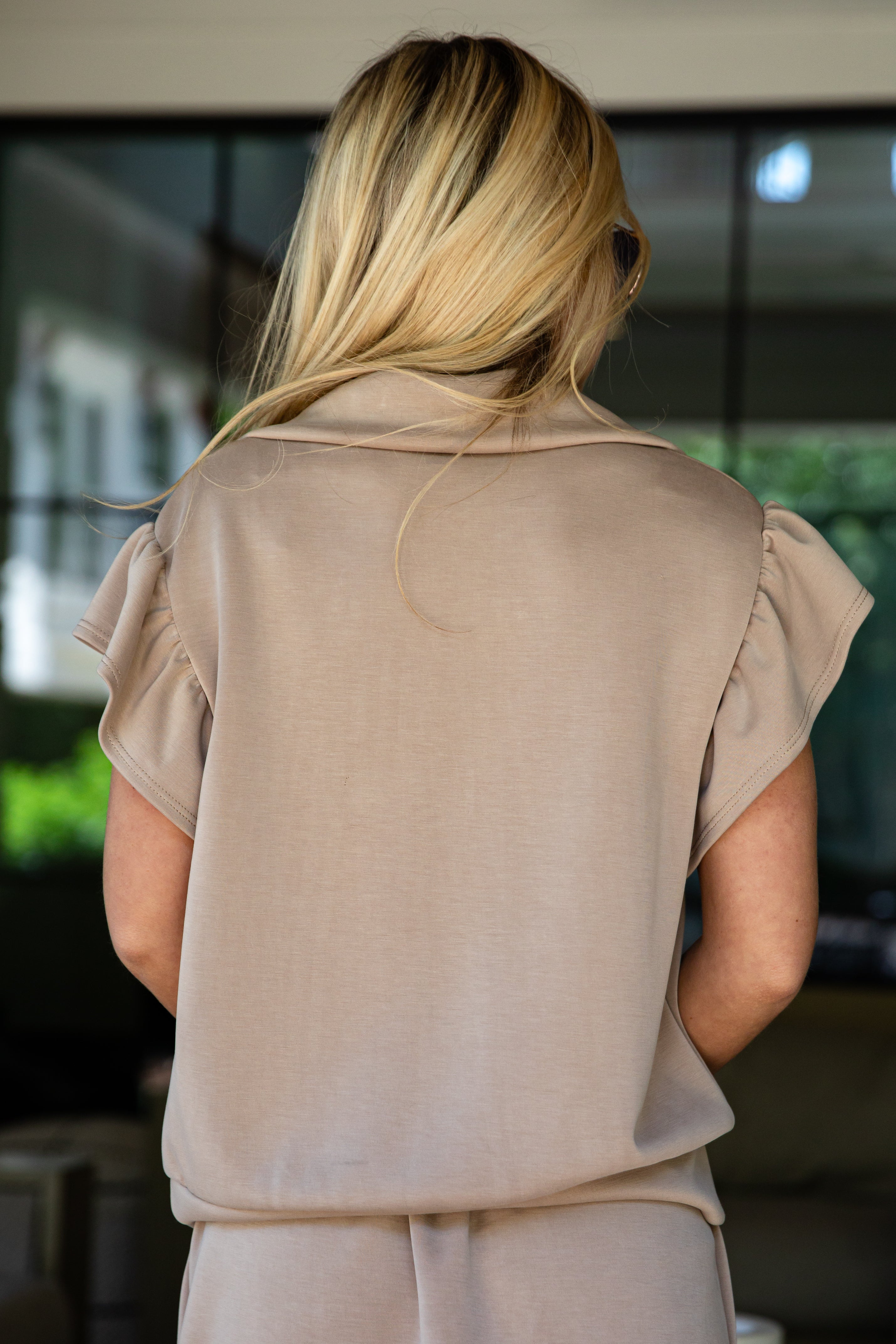 Woman wearing sunglasses and a beige outfit indoors