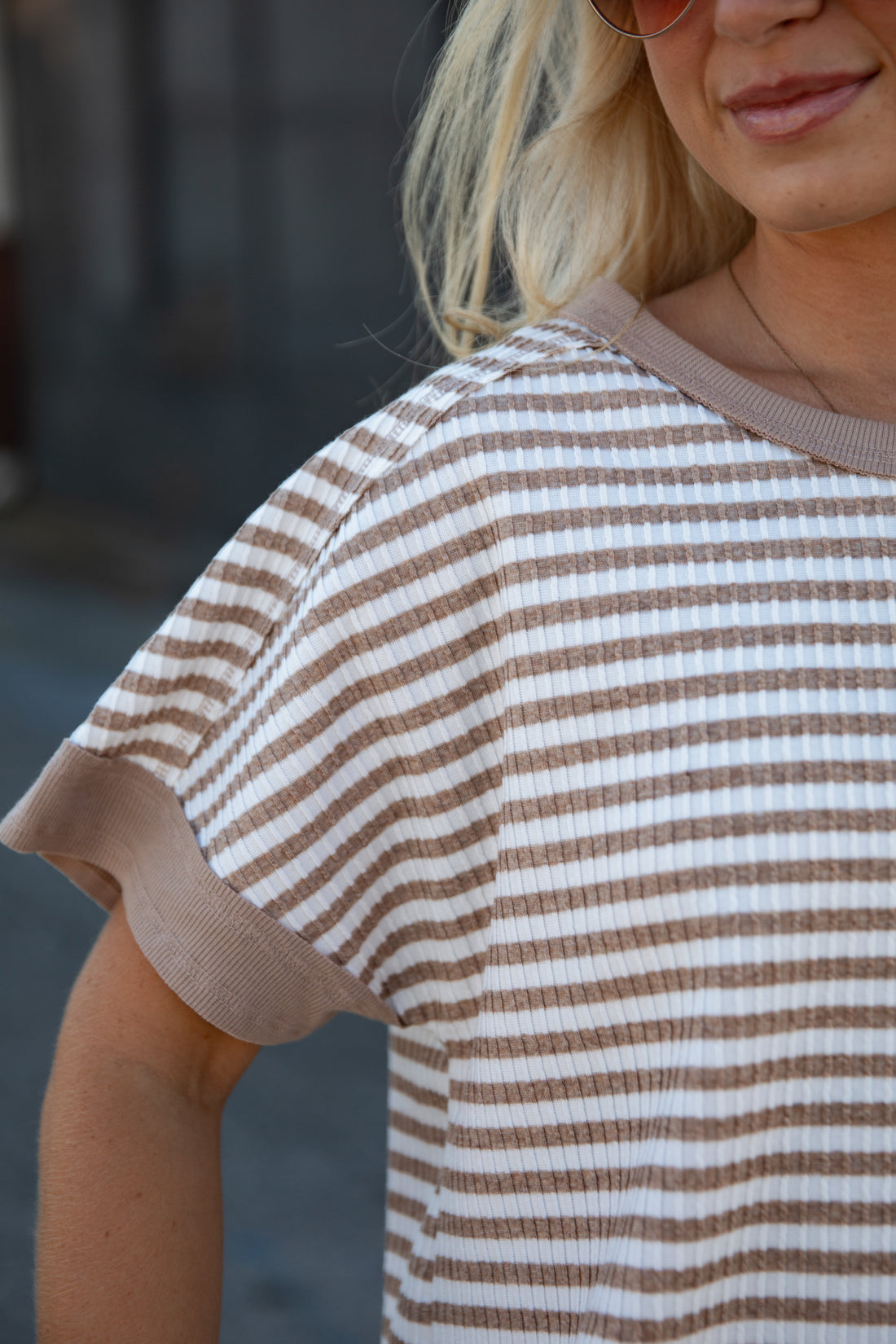 A close-up of a woman wearing a brown and white horizontally striped short-sleeve waffle-knit top with solid brown ribbed trim.