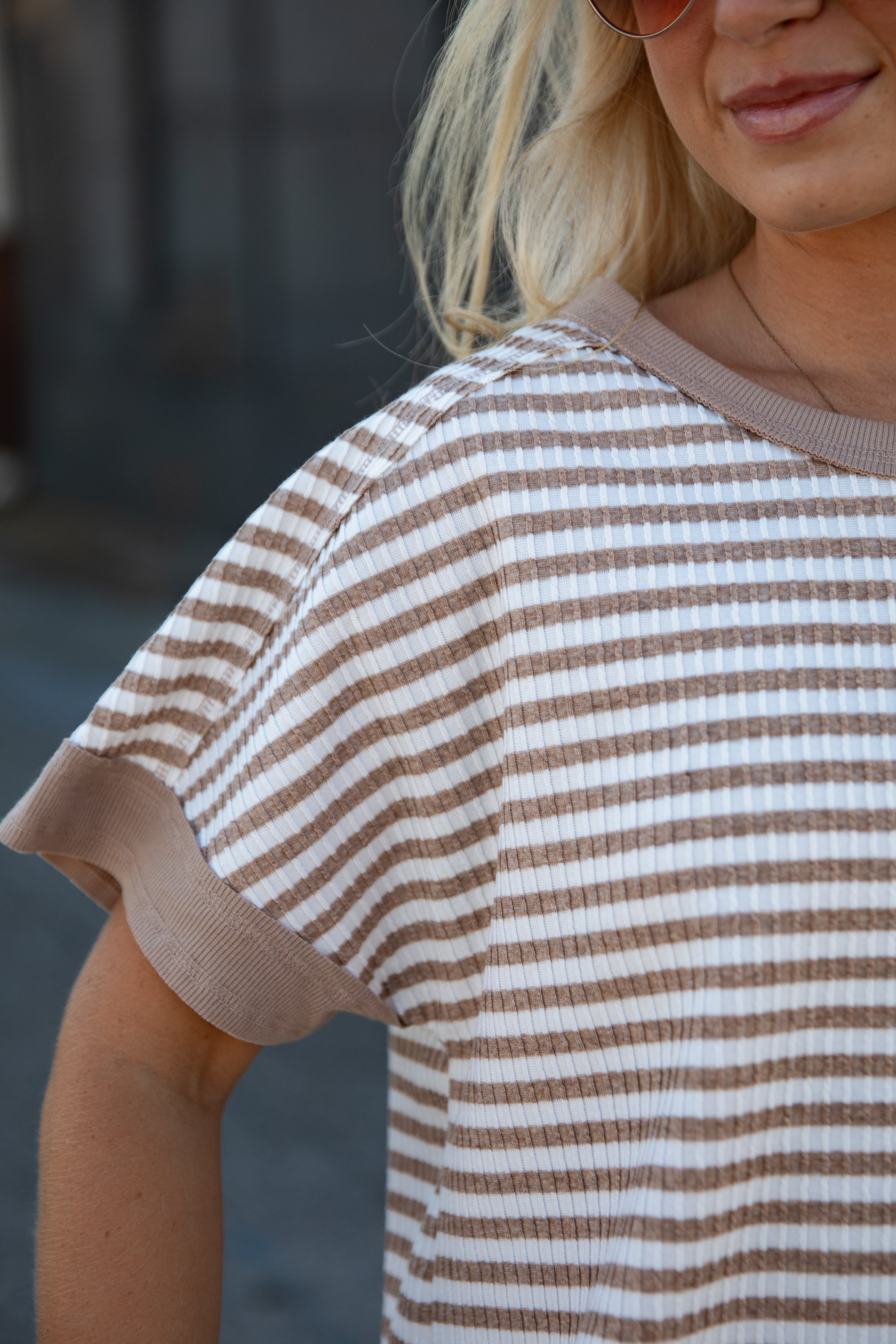 A close-up of a woman wearing a brown and white horizontally striped short-sleeve waffle-knit top with solid brown ribbed trim.