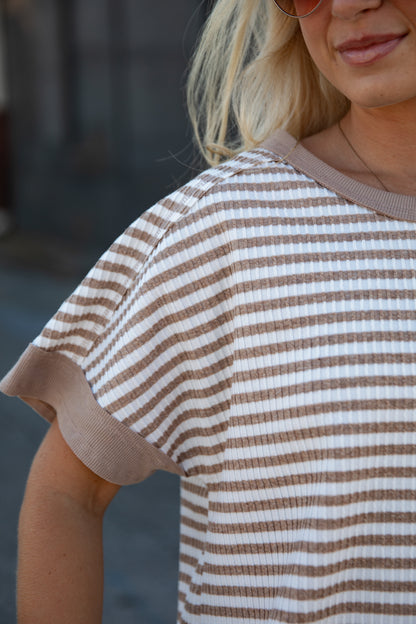 A close-up of a woman wearing a brown and white horizontally striped short-sleeve waffle-knit top with solid brown ribbed trim.