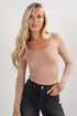 Woman wearing a beige long-sleeve top and black pants on a light gray background