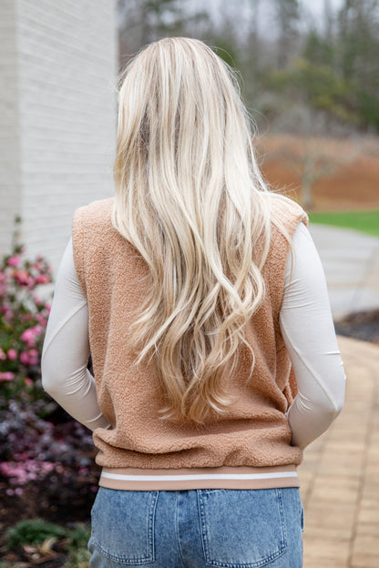 Person wearing a beige vest with long blonde hair, standing outdoors.
