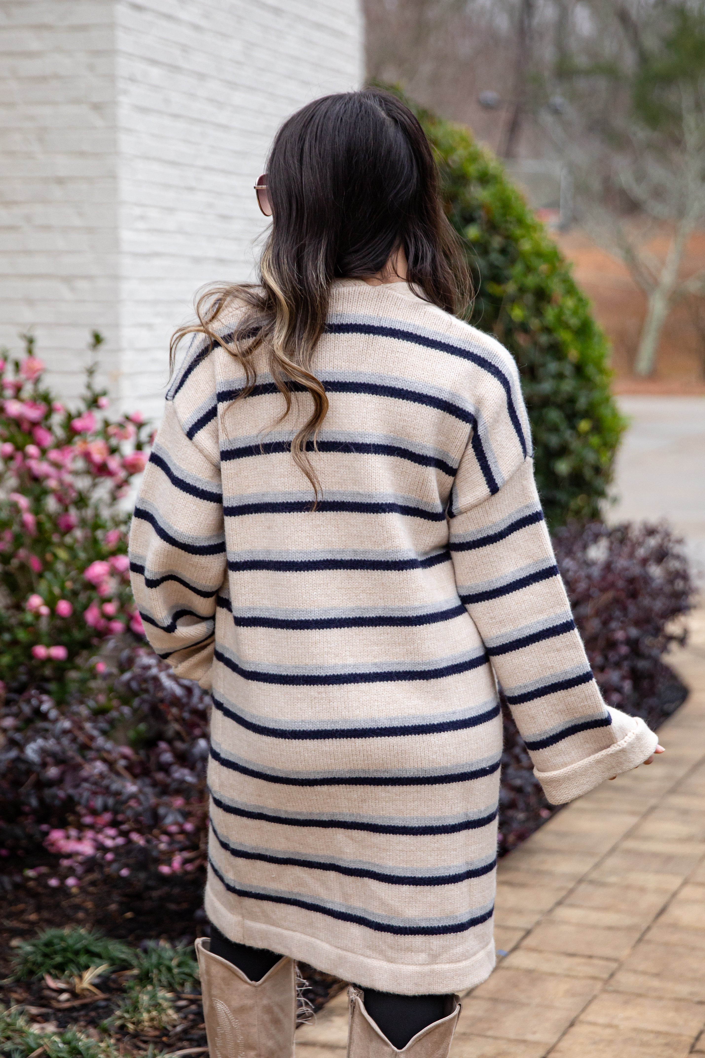 Person wearing a striped coat walking outdoors near a building and plants.