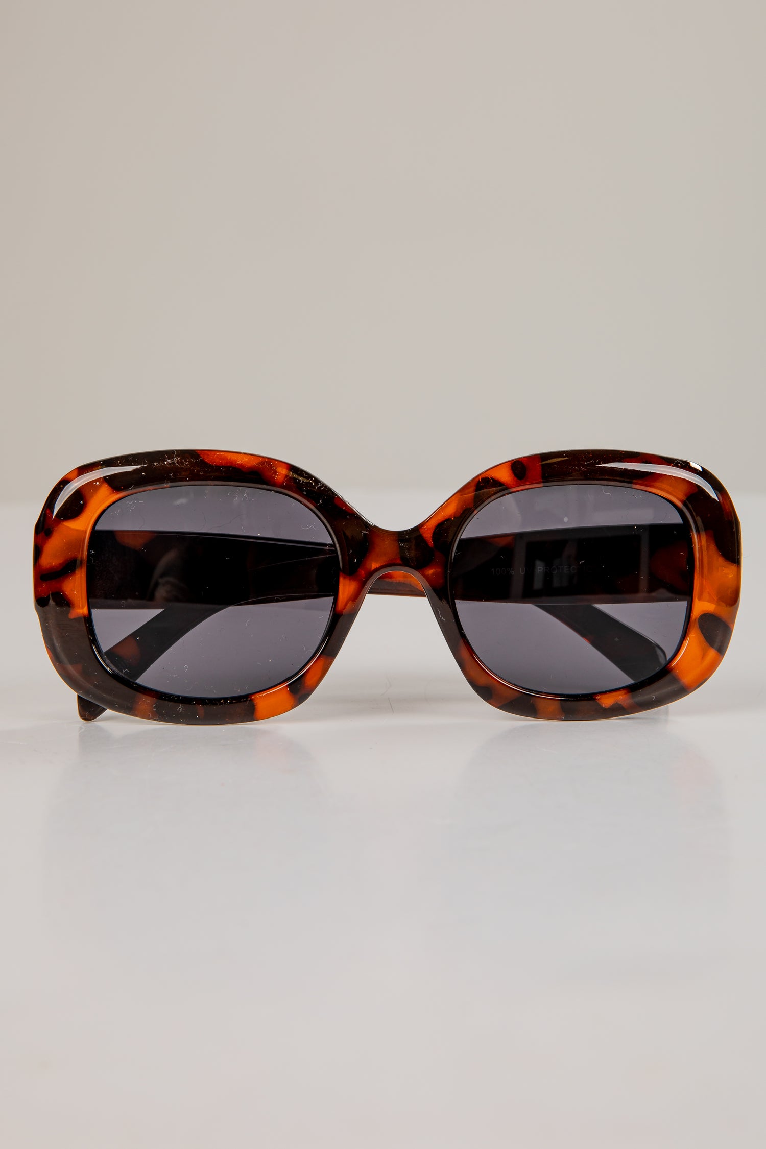 Sunglasses with tortoiseshell frame and dark lenses on a light gray background