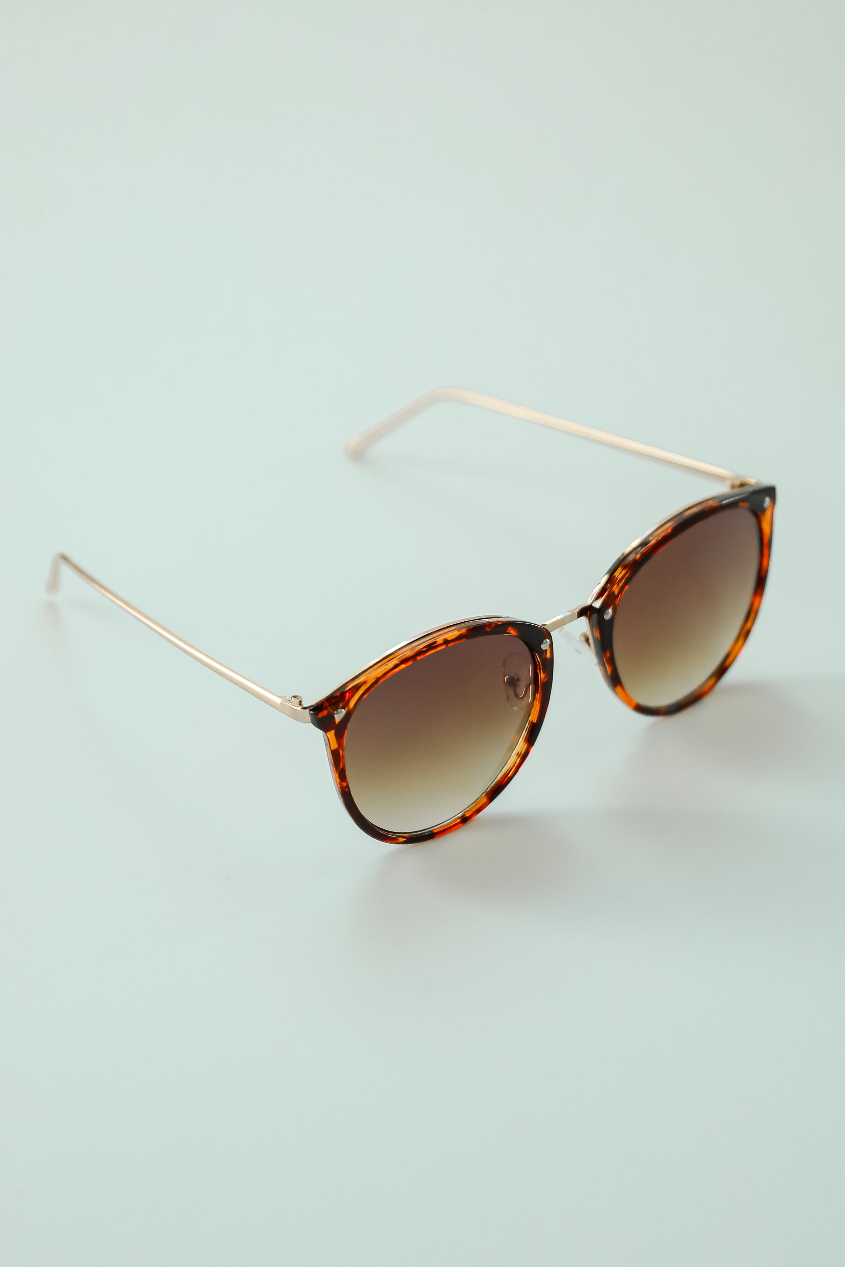 Sunglasses with tortoiseshell frame and gradient lenses on a light blue background